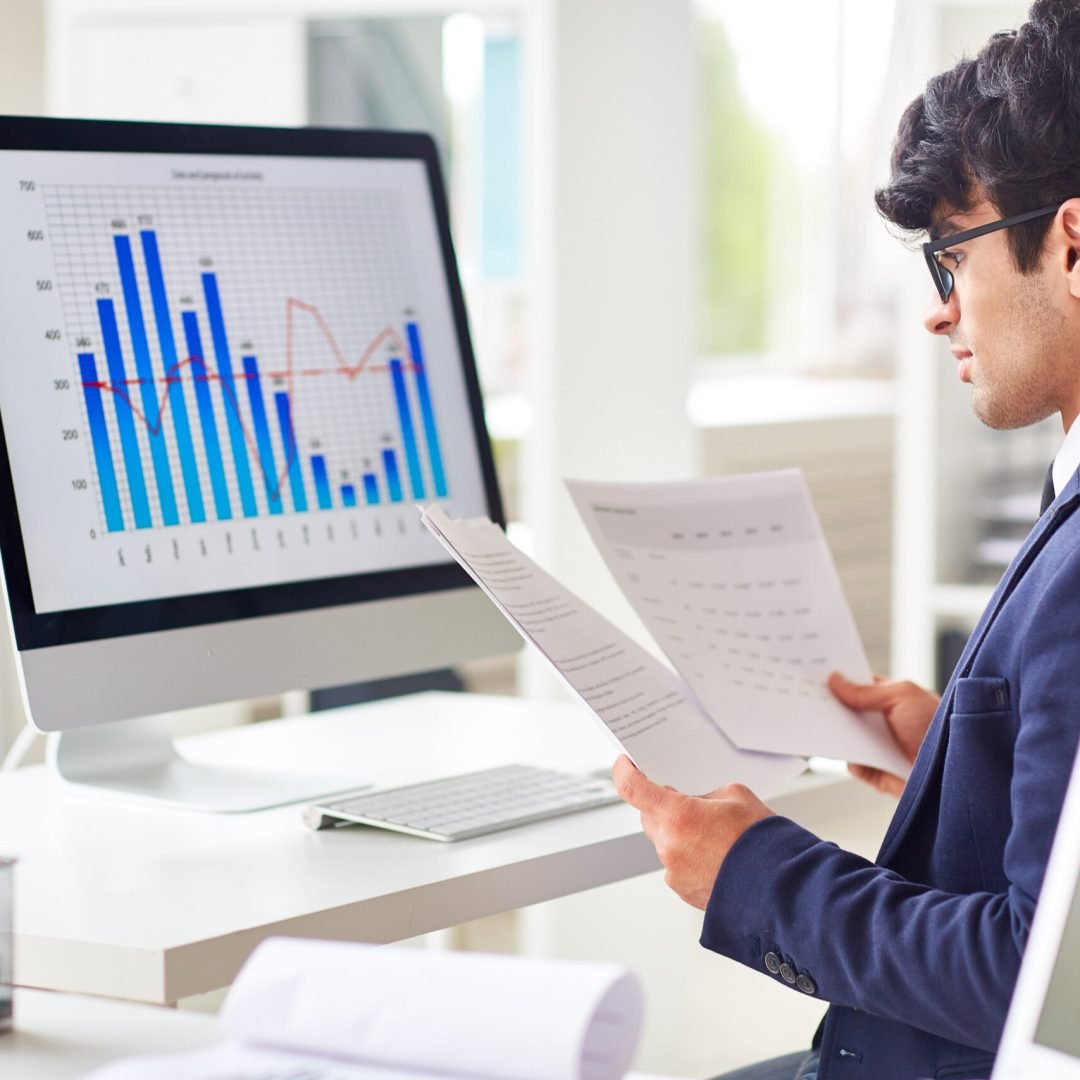 Businessman looking through papers by workplace and analyzing statistics